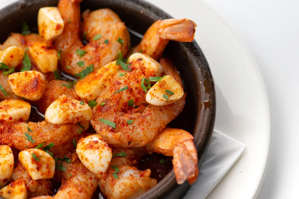 Example photo: Garlic prawns garnished with chopped herbs in a black bowl on a white plate